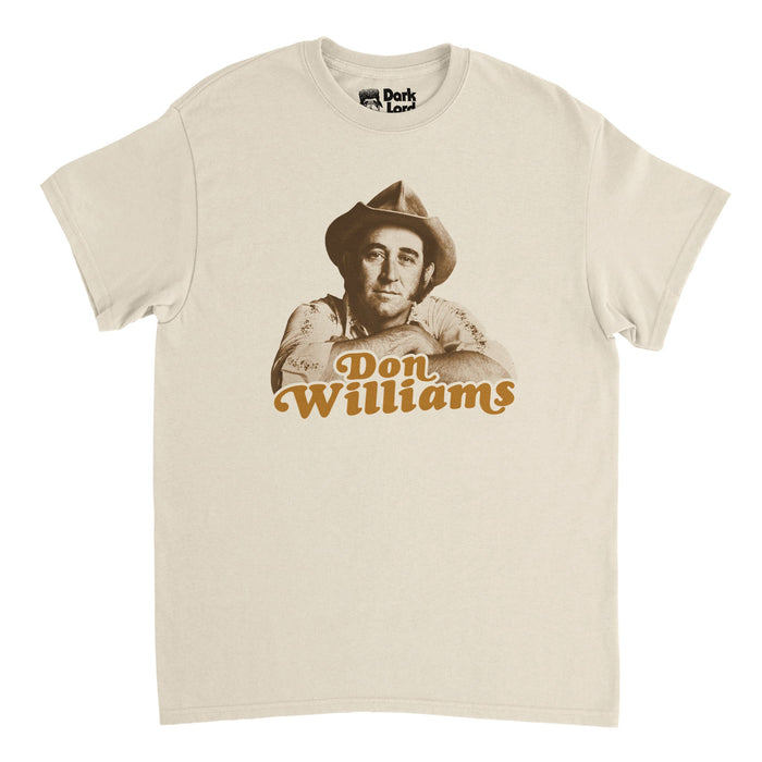 A retro, soft cream 1970s style t-shirt that says "Don Williams" in orange text with an image of the iconic American country music singer and songwriter and actor known as the "Gentle Giant" in the country music scene with hits like "I believe in You", "Tulsa Time", "Love Me Over Again", and "Love Is On A Roll". Also famous for being inducted into the Country Music Hall of Fame and