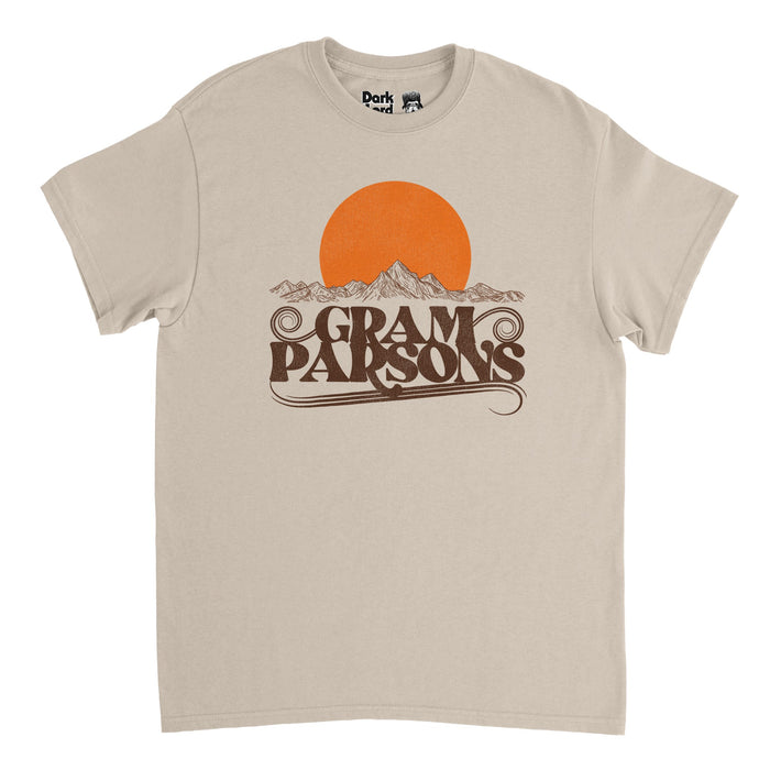 A retro, sand colored t-shirt with a large orange circular sun setting above a beautiful mountain scene drawn in thin lines and sketches. Says "Gram Parsons" in swirly brown letters, in reference to the singer and musician, named Ingram Cicl Connor III, known as "cosmic Cowboy Gram" for his "Cosmic American Music" which came from a mix of country, soul, rhythm and blues, folk, and rock, with hits like "Luxury Liner", "Do You Know How It Feels", "Hickory Wind" with The Byrds, and "Brass Buttons".