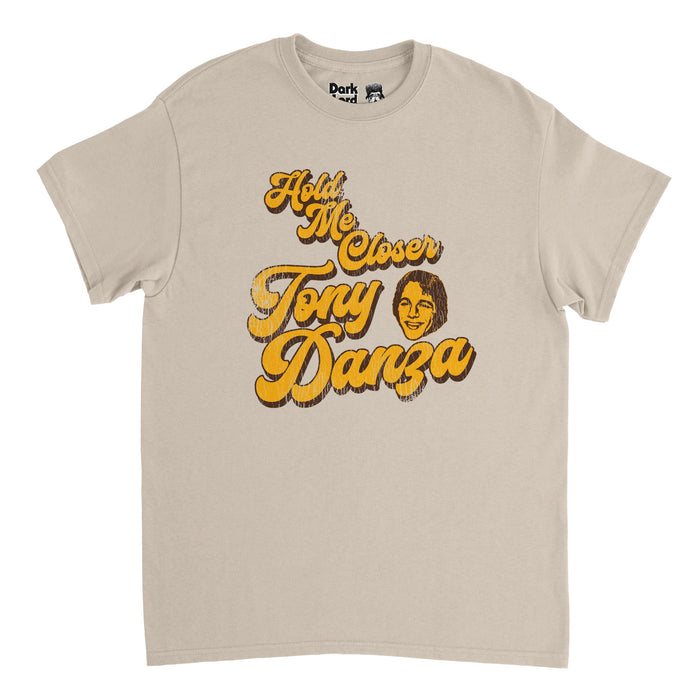 A retro, sand colored vintage light brown shirt that says in yellow bubble letters "Hold Me Closer Tony Danza" with an image of the famous American actor and boxer Tony Danza in yellow. References the song "Tiny Dancer" by Elton John, and the often misquoted lyric "Hold me closer Tiny Dancer", such as when the hilarious character Phoebe (played by Lisa Kudrow) sings the song wrong in the hit show "Friends".