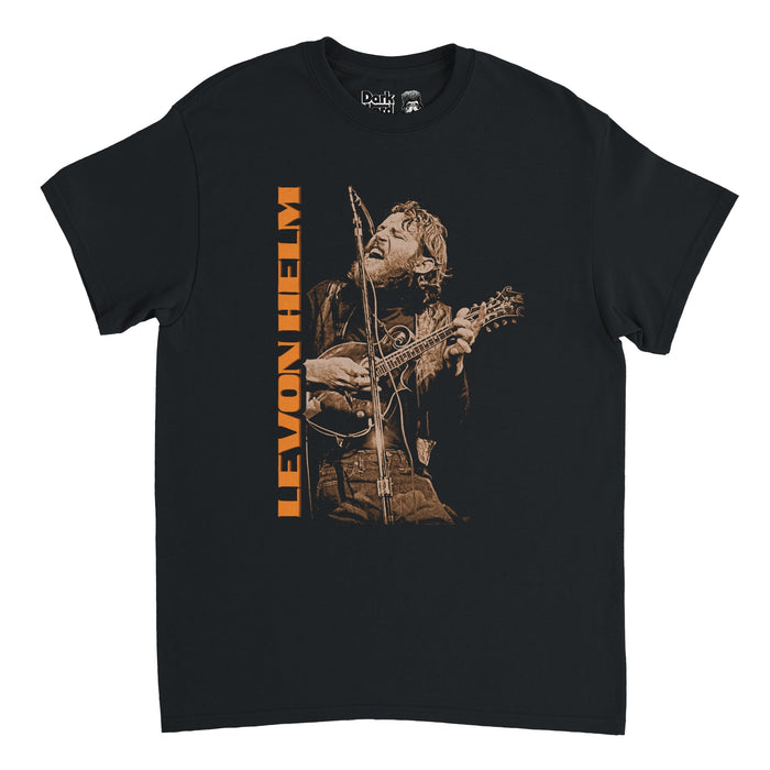 A retro, black short sleeved 80s style t-shirt that says Levon Helm in block orange letters facing sideways beside an image of the iconic musician and drummer, Mark Levon Helm, playing guitar and singing into a microphone onstage.