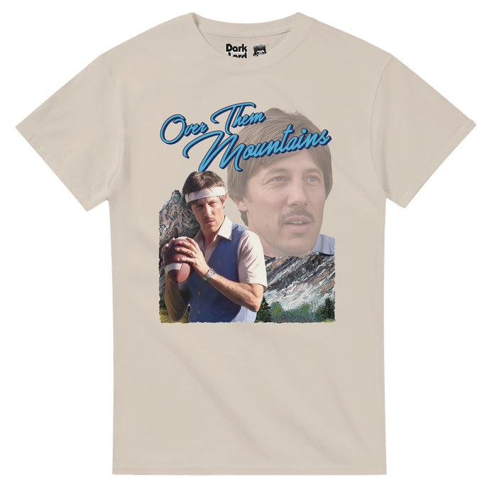 A retro, sand colored off white vintage t-shirt that says "Over Them Mountains" in bright blue text, over an image of the character Uncle Rico staring into the distance & an image of Uncle Rico standing with a football, ready to throw, wearing a white headband, with mountains behind him. References the scene from the 2004 coming of age indie film "Napoleon Dynamite" in which Uncle Rico Dynamite, played by Jon Gries, says "How much you wanna make a bet i can throw a football over them mountains?"