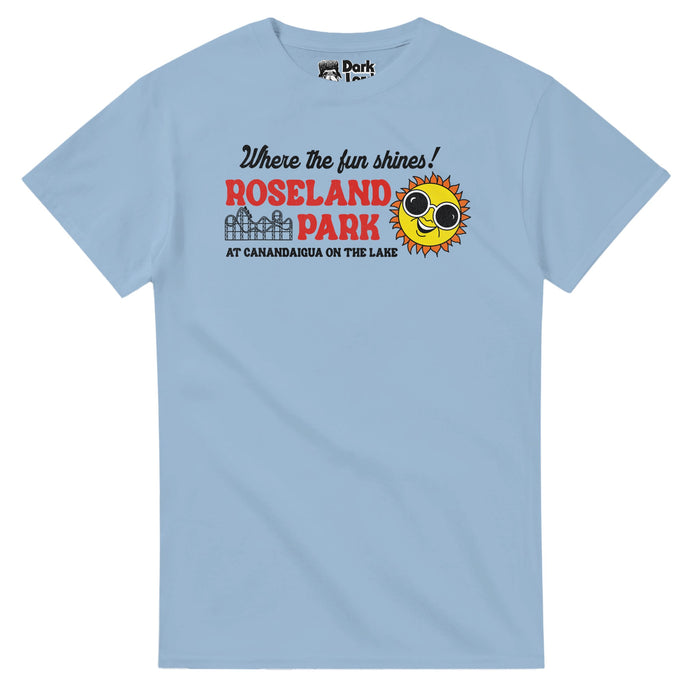 A light blue, vintage 80s style t-shirt that says Roseland Park in bold red text underneath the slogan "Where the fun shines!" and located "At Canandaigua On The Lake" with a rollercoaster graphic and the emblem of a sun with sunglasses and a huge smile. In reference to the amusement park originally called "Lakeside Park" when it opened in 1925 that was a New York staple until it closed in 1985 with tons of fun rides, also known as the "Playground of the Finger Lakes".