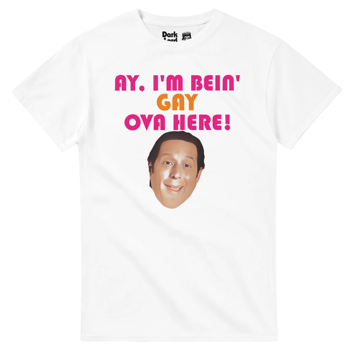 A vintage, 70s style t-shirt in the color white that says 'Ay, I'm Bein' Gay Ova Here!' in orange and pink bright letters above an image of the iconic character Sean Rinaldi, played by the actor Anthony Atamanuik. References the comedy fantasy television series "What We Do in the Shadows" in which this exact shirt was held up by Sean.