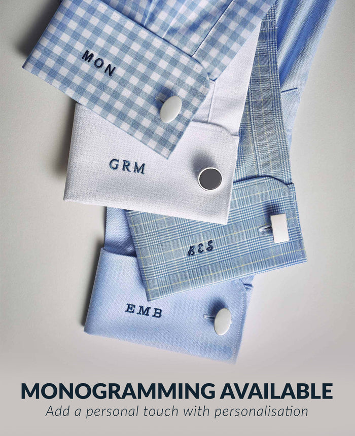 Four personalized shirt cuffs arranged on a light neutral background with promotional text at the top reading 'MONOGRAMMING AVAILABLE' and 'Add a personal touch with personalisation.' The cuffs are shown in light blue, pale blue plaid, white, and blue-and-white gingham, each with a monogram embroidered on the cuff and a button closure visible.