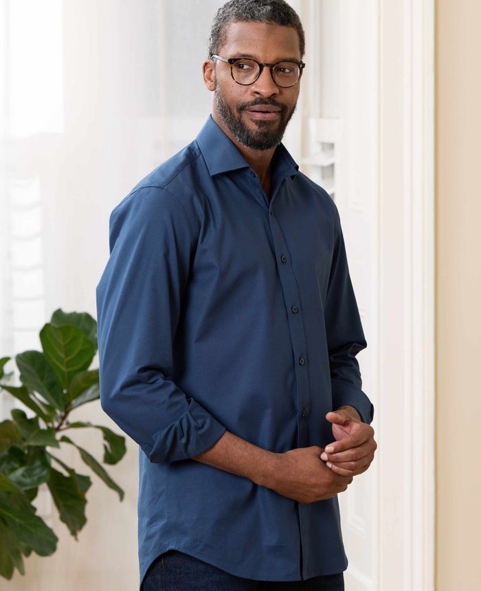 Man wearing a blue shirt standing indoors with a plant in the background