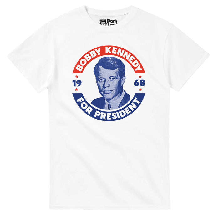 A white colored 80s style t-shirt with a red, white, and blue campaign sticker like graphic of Robert F. Kennedy's face in a blue tint, surrounded by the words "BOBBY KENNEDY FOR PRESIDENt, 1968" with little red stars, and references RFK's run for the Democratic presidential nomination before his assassination in June of 1968, similar to his brother, JFK's, assassination. RFK was known for his role as a lawyer, politician, the 64th United States attorney general, and US Senator from New York.