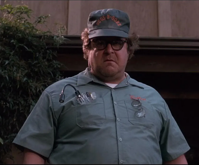 An exterminator, Delbert McClintock, played by John Goodman, wearing a green shirt and a baseball cap with the text "Bugs-B-GONE" on it in the 1990 horror comedy film "Arachnophobia".