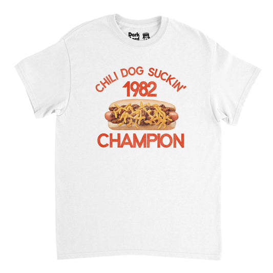 A retro, souvenir t-shirt in the color white that says "Chili Dog Suckin' 1982 Champion" with the image of a hotdog covered in chili and cheese inside a bun. References the iconic John Mellencamp (also known as John Cougar) hit chart topping song "Jack and Diane" in his album American Fool in 1982 in the genre of heartland rock country folk.