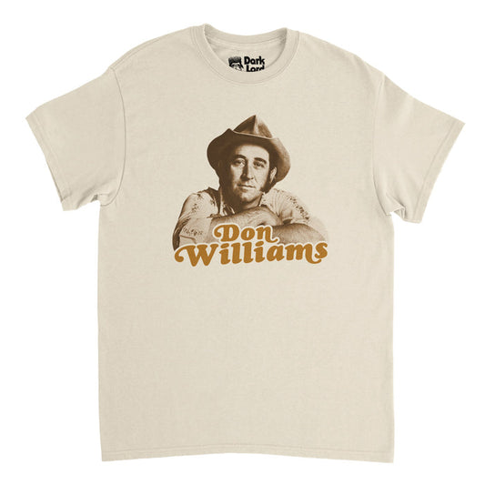 A retro, soft cream 1970s style t-shirt that says "Don Williams" in orange text with an image of the iconic American country music singer and songwriter and actor known as the "Gentle Giant" in the country music scene with hits like "I believe in You", "Tulsa Time", "Love Me Over Again", and "Love Is On A Roll". Also famous for being inducted into the Country Music Hall of Fame and