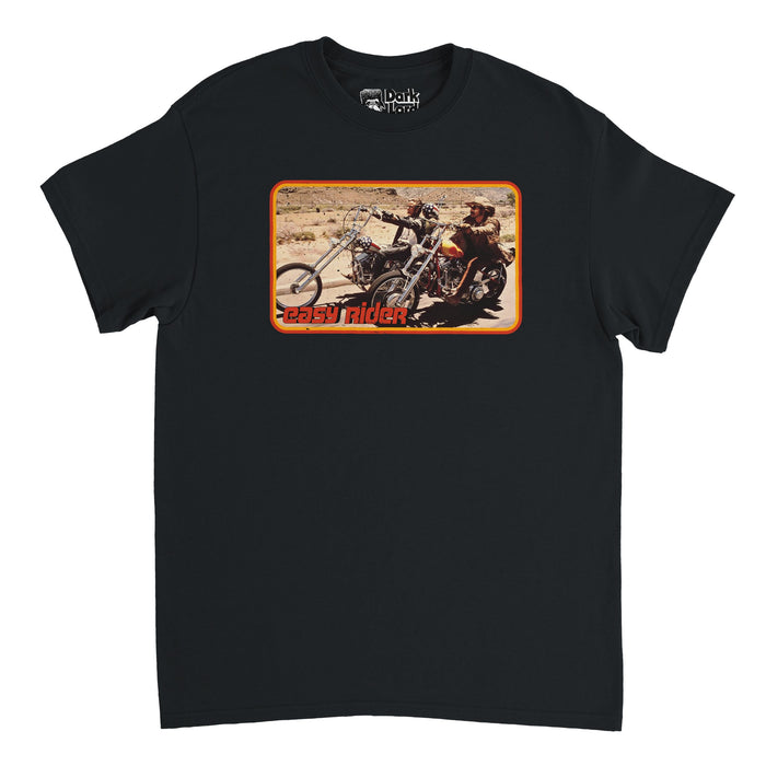 A retro, 70s style black t-shirt with the image of two men riding on motorcycles in the desert, one of the motorcycles covered with American flag symbols, and one of the men wearing a hat. Says "Easy Rider" in red text, reminiscent of the iconic movie where Wyatt, played by Peter Fonda, and Billy, played by Dennis Hopper, ride across the Southwestern United States, reminiscent of the original 1969 film poster.