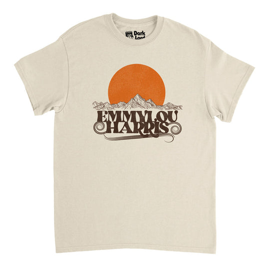 A vintage, soft cream colored 80s style t-shirt that says Emmylou Harris, swirls emanating from the letters aesthetically, with the image of a large, orange sun setting over a drawing of a beautiful mountain range. In reference to the country rock and Americana singer Emmylou Harris, famous in the 70s and 80s, some of her most famous hits including "Boulder to Birmingham", "Together Again", "Red Dirt Girl", and "One of These Days".