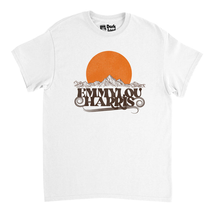 A white, retro 70s style t-shirt that says "Emmylou Harris" in brown text, emphasized by swirling brown lines, under  an image of a drawn mountain range made up of thin brown lines and a large, bright orange sun setting. References the famous country rock and Americana style singer and songwriter with iconic hits like "If This Is Goodbye", "C'est la Vie", "Tusa Queen", and "Roses in teh Snow".
