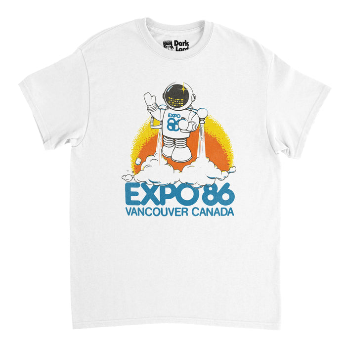 A vintage, 1970s style t-shirt in the color white that says "Expo 86 Vancouver Canada" in blue, referencing the World Fair, formally known as the '1986 World Exposition on Transportation and Communications'. The shirt has a graphic of a robot in a spacesuit using jet propellers pushing white smoke out of them to take off and fly as he waves to the audience, against a backdrop of yellow and orange, in reference to the fair's mascot, called 'Expo Ernie'.