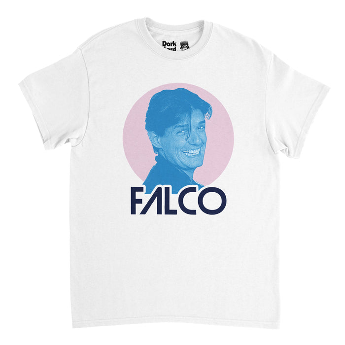 A retro, 70s style shirt in the color white that says "FALCO" underneath an image of a picture of the musician Johann "Hans" Hölzel, also known as his stage name Falco, smiling, his face in the color blue on top of a light pink circle background. References the famous Austrian singer and musician with hits like"Rock Me Amadeus", "Jeanny", "The Sound of Musik", and "Der Kommissar".