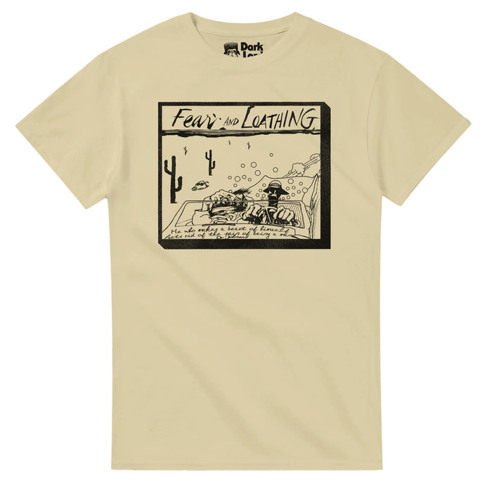 A light brown, sand colored souvenir t-shirt centering a sketched graphic of two guys - characters Raoul Duke and Dr. Gonzo - in a convertible speeding through the Mojave Desert, cacti and a cow with sunglasses in the distance. The shirt says "Fear and Loathing" referencing the 1998 comedic adventure film "Fear and Loathing in Las Vegas", based on Thompson's novel, starring Johnny Depp and Benicio del Toro and the quote "He who makes a beast of himself gets rid of the pain of being a man" by 'Dr