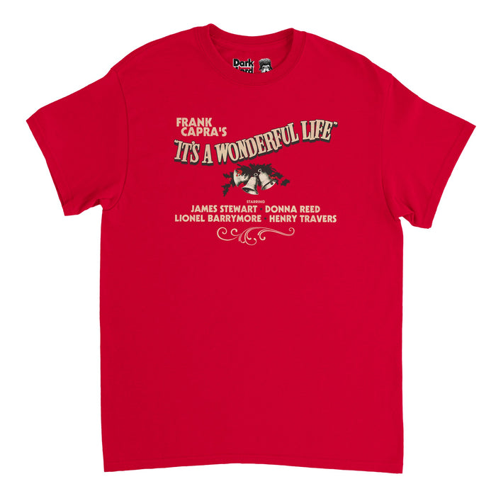 A retro, vintage souvenir bright red colored t-shirt that says 'Frank Capra's It's  A Wonderful Life" and "Starring James Stewart, Donna Reed, Lionel Barrymore, Henry Travers". Includes an image of bells and holly plant and beautiful, magical swirls underneath the famous actors' names. References the classic 1946 family fantasy Christmas film "It's a Wonderful Life" based on "The Greatest Gift" based on "A Christmas Carol" by Charles Dickens.