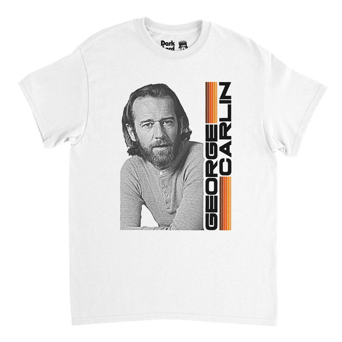 A retro, 80s style t-shirt in the color white that says in sideways black letters "George Carlin", the shirt embellished with tons of warm toned lines in purple, orange, and yellow. Includes a black and white image of George Carlin, the iconic American stand-up comedian, actor, social critic, and author, known for dark comedy and political ideologies and created The George Carlin Show.