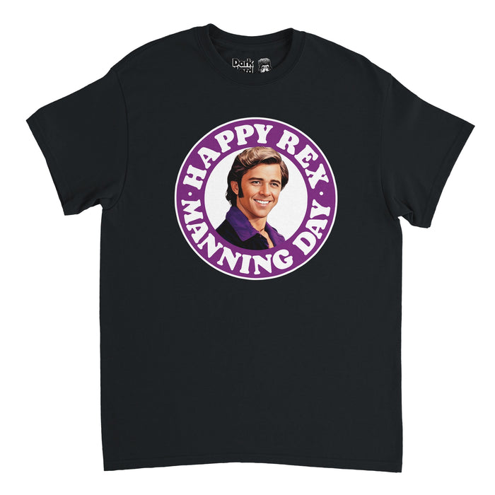 A vintage, 70s souvenir t-shirt in the color black with an image of actor Maxwell Caulfield as the heartthrob singer character Rex Manning from the iconic cult classic film "Empire Records", wearing a purple shirt and necklace, surrounded by a circular purple band that says Happy Rex Manning Day which references April 8th, the day the movie is set, and honors legendary singer Kurt Cobain.