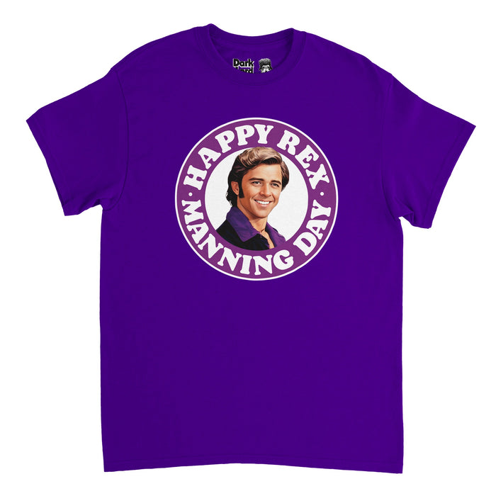 A dark purple souvenir, 90s style t-shirt that says "Happy Rex Manning Day" in a purple circle surrounding an image of actor Maxwell Caulfield playing the character Rex Manning in the cult classic movie "Empire Records", his hair slicked back in a side part, side burns down his face, smiling, with his iconic purple button up shirt collar popping out over his suit jacket and open to show his necklace. The day, April 8, is when the movie is set and honors famous icon and singer Kurt Cobain.