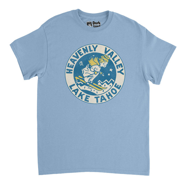 A retro, 70s style light blue t-shirt with the retro logo of Heavenly Mountain Resort, a popular skiing and snowboarding destination overlooking the stunning Lake Tahoe with ski runs in both California and Nevada in the Sierra Nevada Mountain Range. The logo says "Heavenly Valley" and "Lake Tahoe" and includes the image of an angle skiing downhill in a white dress with golden angelic wings, a halo, and yellow skis.