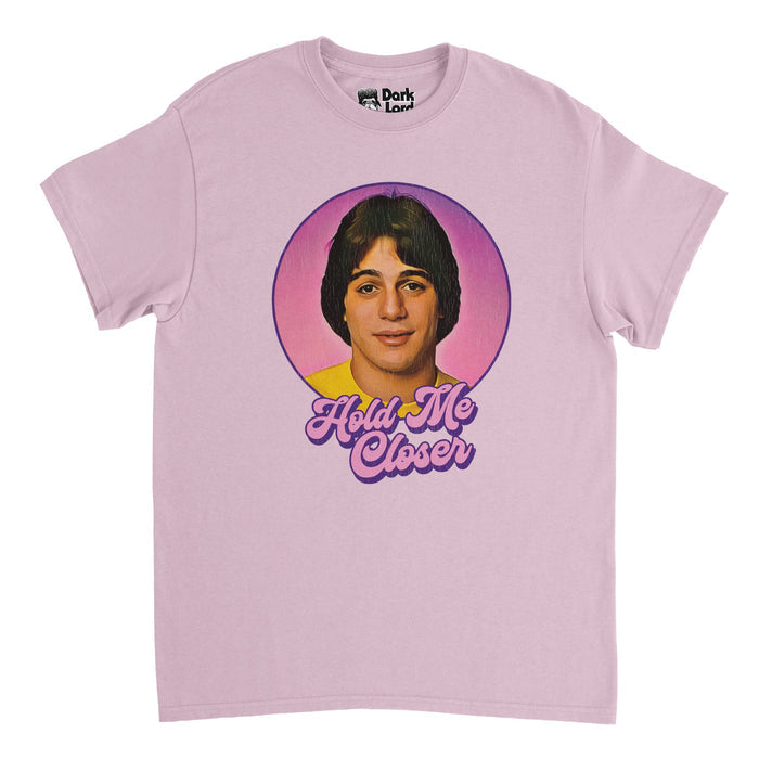 A retro, 80s style light pink t-shirt that says "Hold Me Closer" in purple and pink bubble letters beneath an image of actor and retired professional boxer Tony Danza, famous for his role on sitcom "Who's the Boss?". References the Elton John song "Tiny Dancer" with lyrics often misheard as "Hold me closer, Tony Danza" or "Hold me close young Tony Danza", famously quoted by character Pheobe in an episode of the American television sitcom "Friends".