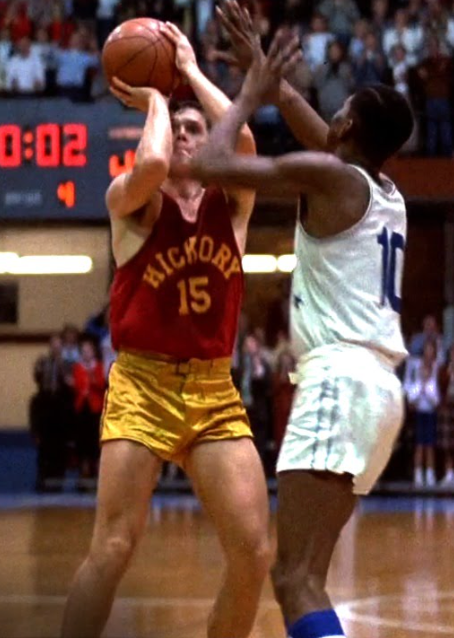Two basketball players, one wearing a dark red maroon jersey with the name "Hickory" and number "15" in yellow, another with a white and navy blue jersey and the number "10". References the character Jimmy Chitwood, played by Maris Valainis, in the 1986 sports film "Hoosiers" about an Indiana high school's basketball championship.