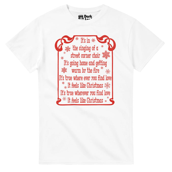 A vintage, 80s style white colored short sleeved t-shirt that says "It's in the singing of a street corner choir, It's going home and getting warm by the fire, It's true where ever you find love, It feels like Christmas, It's true wherever you find love, It feels like Christmas" in red letters, adorable snowflake graphics surrounding the words within a red ribbon line box. References the song "It Feels Like Christmas" by Ghost of Christmas Present from 1992 family musical "The Muppet Christmas C