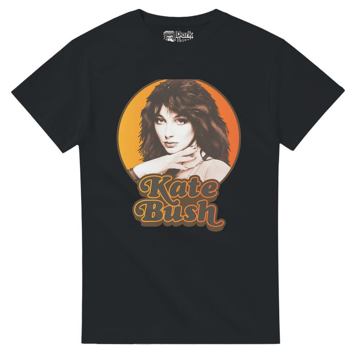 A vintage black colored 80s style t-shirt that says "Kate Bush" in gray text underneath an image of the iconic singer and songwriter looking straight at the camera, her hair dark brown, her hand on her neck, against an hombre yelllow/orange background. References the English singer, dancer, and producer known for her eclectic music style, popular in the 1980s-1990s with 25 UK top 40 singles and hits like "Running Up That Hill", "The Man with the Child in His Eyes",  "Babooshka", and "There Goes