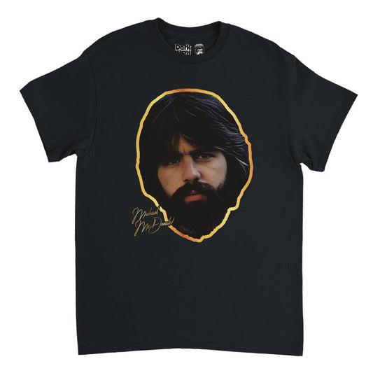 A retro, souvenir black short sleeved t-shirt that says "Michael McDonald" in gold text with an image of the iconic singer and songwriter's face, framed by his dark black brown thick hair and beard and surrounded by a gold outline. Known for being the lead vocalist of the Doobie Brothers rock band and a backing vocalist for Steely Dan.
