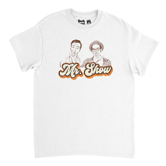 A vintage, 70s style white colored short sleeved t-shirt that says "Mr. Show" in cursive bubble letters with outlines of brown and orange colors and includes the image of two men, sketched out in brown colors, posing with their hands and making silly faces, one wearing glasses, a plaid flannel, and a bowler hat, the other a button up shirt. In reference to the hilarious 1995 sketch comedy television series called "Mr. Show with Bob and David" which starred comedians Bob Odenkirk and David Cross.