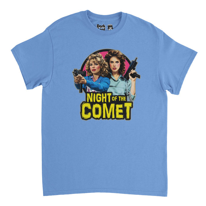 A retro, 80s style blue t-shirt that says Night of the Comet in yellow, Halloween font text below an image of two beautiful women, the heroines, one blonde and one brunette, holding guns against a pink circular backdrop. References the iconic 1984 science fiction comedy horror film "Night of the Comet" starring Kelli Maroney and Catherine Mary Stewart as Samantha "Sam" Belmont and Regina "Reggie" Belmont about comets and zombies.