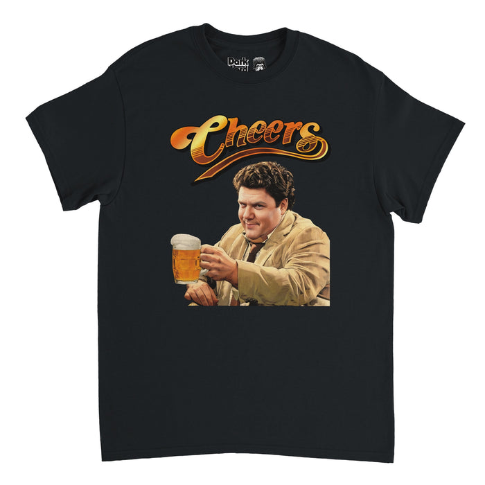 A vintage, black colored 90s style short sleeved t-shirt that says "Cheers" in orange, brown, and yellow hombre colors, in reference to the famous 1982 sitcom of the same name. Includes the image of a man with curly brown hair raising his pint of beer in a beer mug, wearing a light brown jacket and a tie, smiling, the character Norm Peterson played by iconic actor George Wendt.
