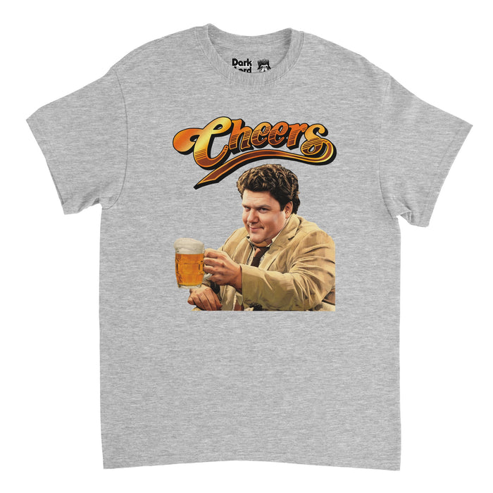 A heather gray 80s style souvenir t-shirt that says "Cheers" in hombre yellow and orange shaded text above an image of iconic actor George Wendt as character Norm Peterson on the hilarious NBC sitcom "Cheers" wearing a light brown trench coat, holding a glass mug of beer filled to the top.