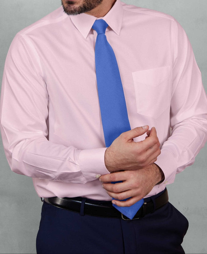 A man wearing a light pink long-sleeve dress shirt, a bright blue tie, and navy trousers, standing against a textured gray studio background.