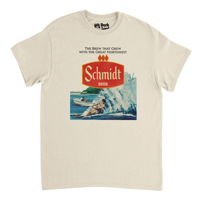 A soft cream colored souvenir, 80s style t-shirt with the red logo of "Schmidt Beer" underneath text saying "the brew that grew with the great northwest", referencing the original Minnesota macro lager beer. Includes an image of a man waterskiing, water spurting from behind him, a motorboat in the distance, referencing the vintage water skiing design on Schmidt Beer Can Nature Series.