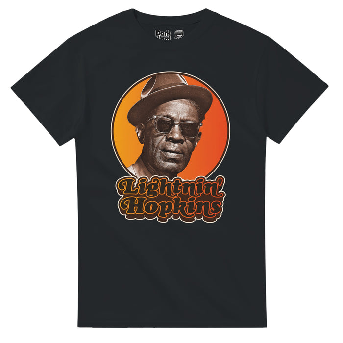 A retro, 80s style souvenir black colored t-shirt that says "Lightnin' Hopkins" in black text outlined in hombre yellow to red neon colors, an image of him wearing sunglasses and a hat against a yellow and orange bright circular background. References the blues singer, songwriter, and guitarist Samuel John "Lightnin" Hopkins, known as one of the 100 greatest guitarists of all time, and for hits like "Leavin' Blues", "Feel So Bad", "T-Model Blues", "Shake That Thing", and "I'm Leaving You Now".