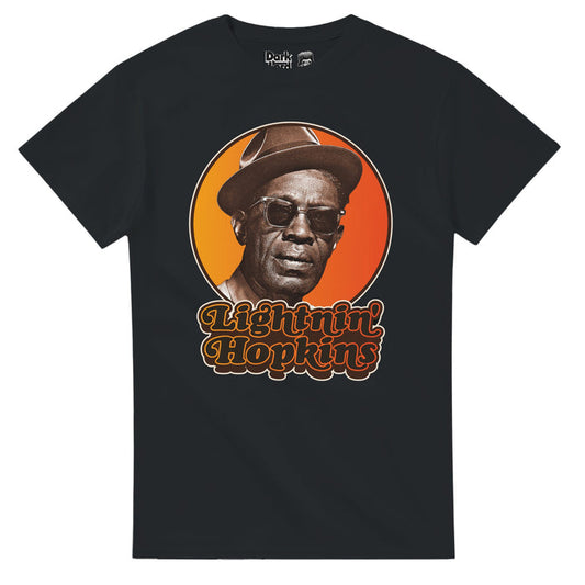 A retro, 80s style souvenir black colored t-shirt that says "Lightnin' Hopkins" in black text outlined in hombre yellow to red neon colors, an image of him wearing sunglasses and a hat against a yellow and orange bright circular background. References the blues singer, songwriter, and guitarist Samuel John "Lightnin" Hopkins, known as one of the 100 greatest guitarists of all time, and for hits like "Leavin' Blues", "Feel So Bad", "T-Model Blues", "Shake That Thing", and "I'm Leaving You Now".