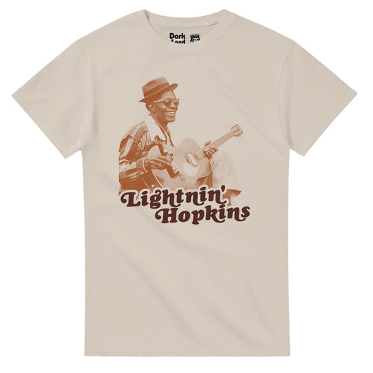 A retro, sand colored, 80s style short sleeved t-shirt that says "Lightnin' Hopkins" underneath the image of the iconic country blues singer, songwriter, and guitarist,  wearing a hat, sunglasses, and a plaid shirt, a guitar in his hands, in a sepia toned color. References the blues icon Samuel John "Lightnin" Hopkins with famous hits like "Mojo Hand", "Baby Please Don't Go", "Lightnin' Boogie", and "Trouble in Mind", and one of the top 100 guitarists of all time according to Rolling Stone Magaz