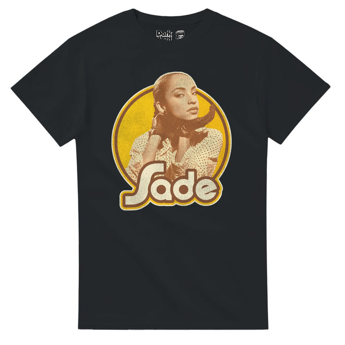A souvenir, black colored 80s style t-shirt with a sepia toned image of the Nigerian-British singer and songwriter Sade Adu - known as one of the most successful female artists from Great Britain - highlighted on a circular yellow background above the word "Sade", referencing not just her name but the band she created in the 1980s, also includign Stuart Matthewman, Andrew Hale, Paul Cooke, and Paul Denman, with famous songs like 'Smooth Operator', 'Cherish the Day', 'By Your Side', & 'No Ordinar