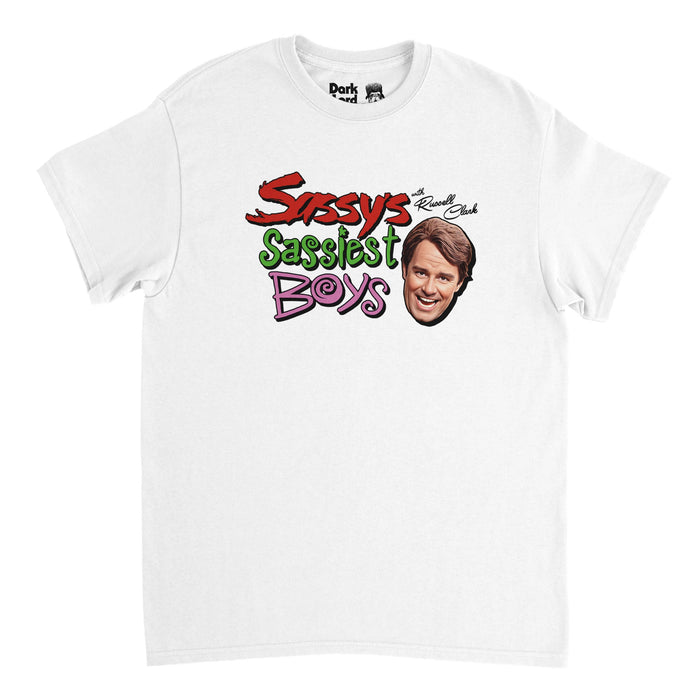 A white colored, 80s style souvenir t-shirt that says "Sassy's Sassiest Boys" in red, green, and pink, and "with Russell Clark" in cursive to the side above an image of the head of the character smiling, played by comedian Phil Hartman on SNL during the skit all about interviewing sassy boys, like Christian Slater.