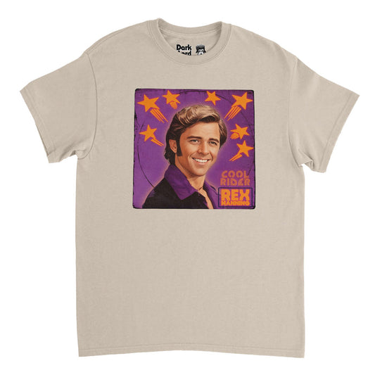 A retro, 80s style soft cream sand colored t-shirt with an image of actor Maxwell Caulfield playing character Rex Manning with his iconic sideburns, slicked back side part hair, and purple button up shirt on a background of purple with orange shooting stars. Says Cool Rider, referencing the cult classic film "Grease 2", and Rex Manning, referencing the coming of age movie "Empire Records".