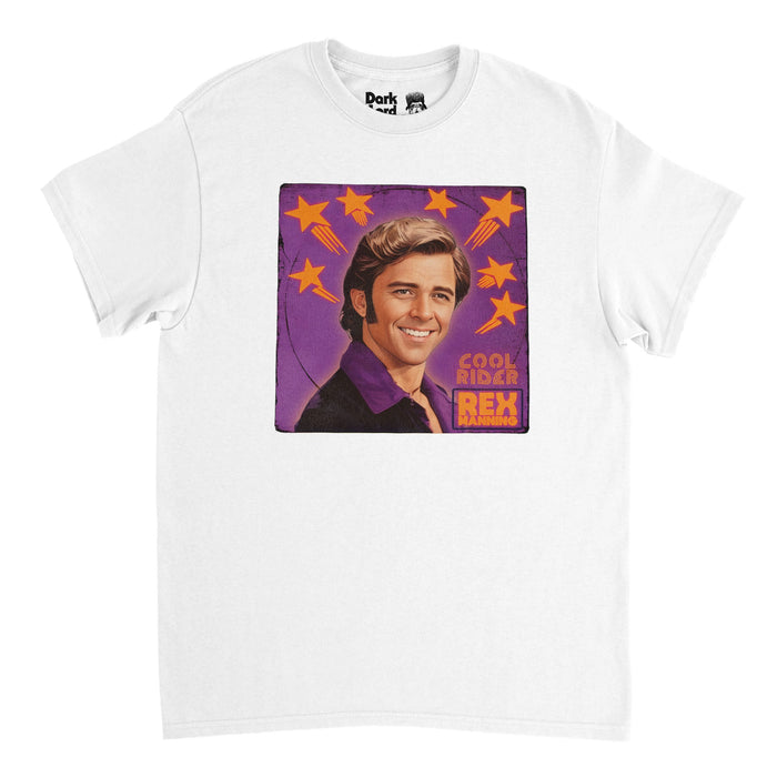 A vintage, white colored 80s style t-shirt with an image of actor Maxwell Caulfield as character as character Rex Manning, wearing his iconic shiny purple shirt and suit with slicked black hair and sideburns over a purple background filled with bright orange shooting stars surrounding his head. The shirt says "Cool Rider" and "Rex Manning" referencing Rex Manning Day and the coming of age comedy drama film "Empire Records" as well as the cult classic "Grease 2".