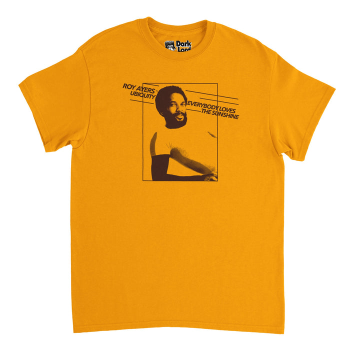 A retro, 70s style orange colored t-shirt with an image of iconic singer and vibraphonist Roy Ayers and the words "Roy Ayers Ubiquity", his band, and "Everybody Loves the Sunshine", his top hit song and album from 1976. The image on the shirt is highly reminiscent of the cover of the album Everybody Loves The Sunshine.