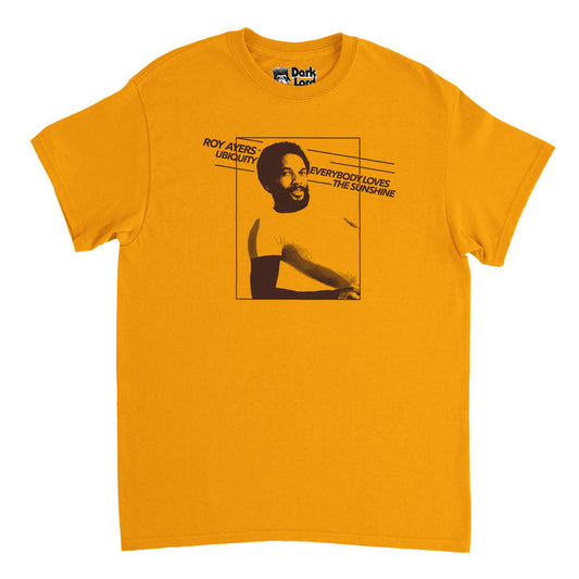 A retro, 70s style orange colored t-shirt with an image of iconic singer and vibraphonist Roy Ayers and the words "Roy Ayers Ubiquity", his band, and "Everybody Loves the Sunshine", his top hit song and album from 1976. The image on the shirt is highly reminiscent of the cover of the album Everybody Loves The Sunshine.
