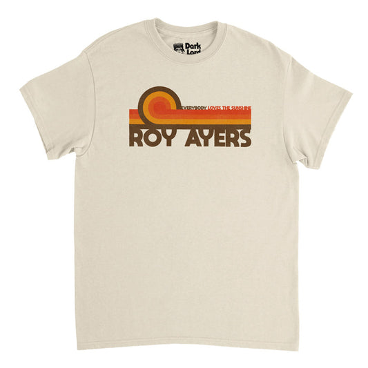A soft cream colored vintage, 90s style t-shirt that says "Roy Ayers" in brown letters, referencing the famous R&B and jazz singer who revolutionized jazz-funk and was key in the acid jazz movement, nicknamed the "Godfather of Neo Soul". Above his name are multicolored stripes - red, orange, yellow and brown - and the title of his most famous album: Everybody Loves The Sunshine.