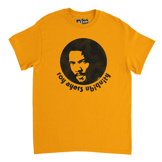 A retro, 80s style light orange t-shirt that says "roy ayers ubiquity" under a black and white image of the iconic singer, musician, and vibraphonist himself. In reference to Roy Ayers' band, with whom he released his most famous album and song "Everybody Loves the Sunshine", and the same shirt he wore to perform at the Kool Festival in Cincinnati in 1976 right after the release of the iconic album.