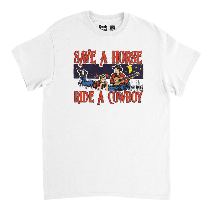 A vintage, white colored 80s style shortsleeved t-shirt that says "Save a Horse, Ride a Cowboy" in capitalized bold red text with the image of a man with a guitar and cowboy hat serenading a woman laying in the grass, both wearing red plaid shirts, jeans, and cowboy boots at night time, stars and the yellow moon in the distance. In reference to the famous country music duo Big & Rich and their iconic hit song 'Save a Horse (Ride a Cowboy' from the year 2004.