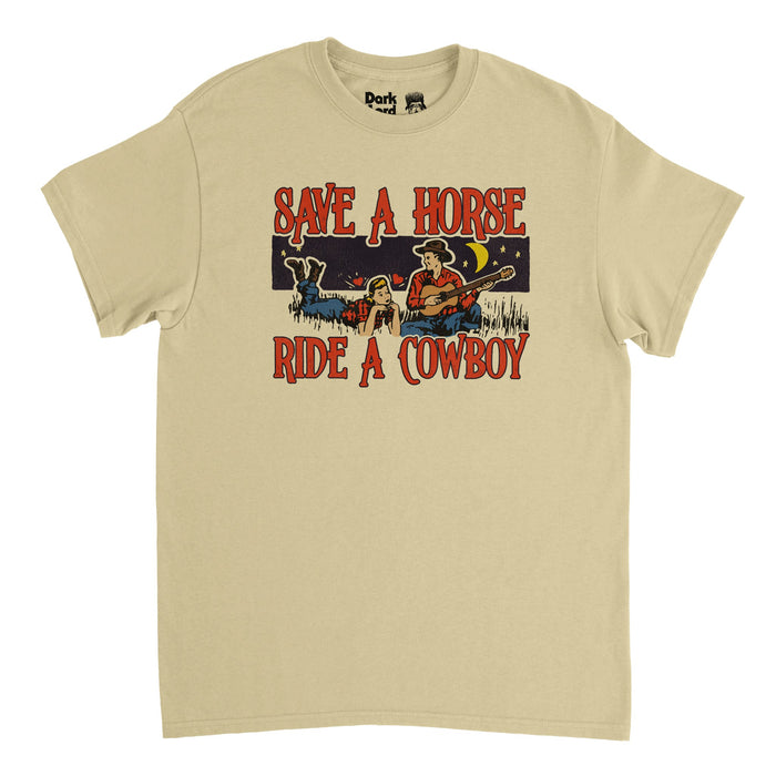 A retro, sand colored vintage soft cream t-shirt that says "Save a Horse, Ride a Cowboy" in red text, surrounding the image of a man serenading a woman laying in the grass with a guitar, wearing red shirts, blue jeans, and cowboy boots and a cowboy hat in front of a moon and star filled night sky. References the famous 2004 song "Save a Horse (Ride a Cowboy" by country music duo Big & Rich
