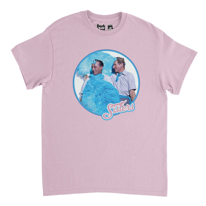 A retro pink colored 70s style t-shirt with the image of two men with huge blue feathers and small blue headbands wearing button up shirts smiling, surrounded by a blue circle, above the word "Sisters" in pink letters. References the iconic scene from the movie "White Christmas" in which Bing Crosby and Danny Kaye as Bob Wallace and Phil Davis lip sync to the song "Sisters" while wearing feminine clothing.