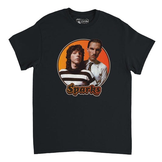 A black colored, 80s style retro t-shirt that says "Sparks" in hombre yellow/orange outlined bubble letters. Has an image of the two brothers Ron and Russell Mael from the popular cult pop-rock band Sparks, one with long hair wearing a striped black and white shirt, the other a tie on a crisp white button up, on top of an hombre yellow to orange circular backdrop, known for their song 'This Town Ain't Big Enough for Both of Us' and for the documentary "The Sparks Brothers".
